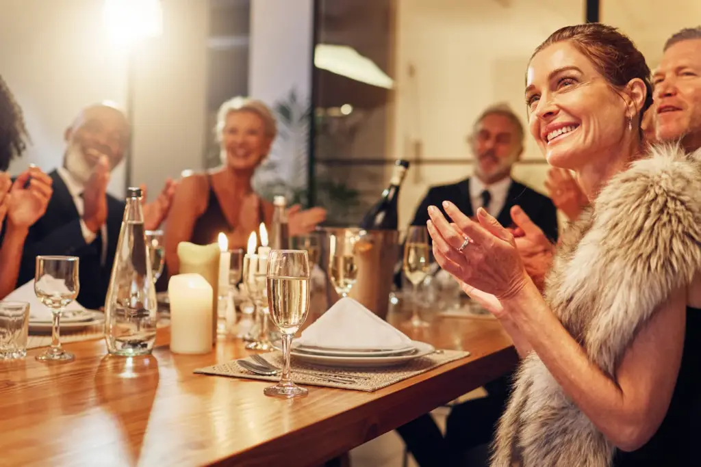 Guests in evening dress applauding at a candlelit dinner table set with champagne glasses
