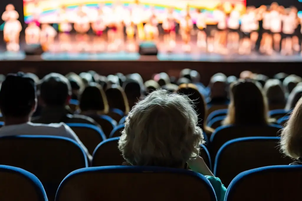 An audience seated in rows in a darkened theatre, watching a brightly lit stage performance