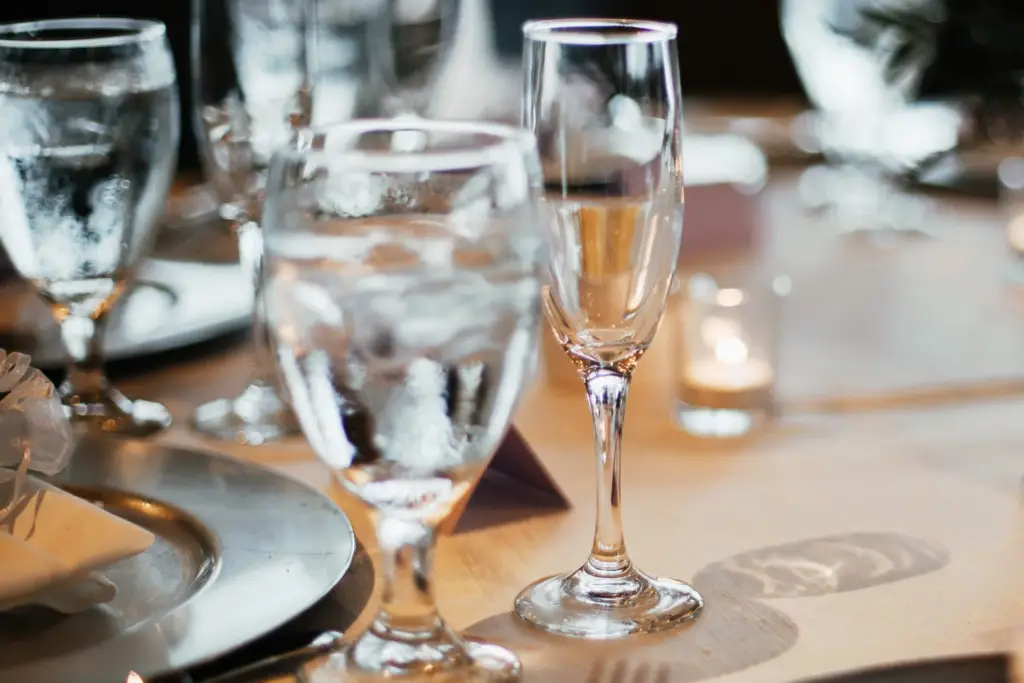 Water and champagne glasses, a charger plate and a lit candle on a set table in warm light